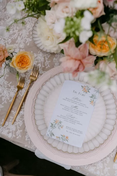 Close-up of a floral wedding menu on a scalloped plate surrounded by fresh roses at Euridge Manor.