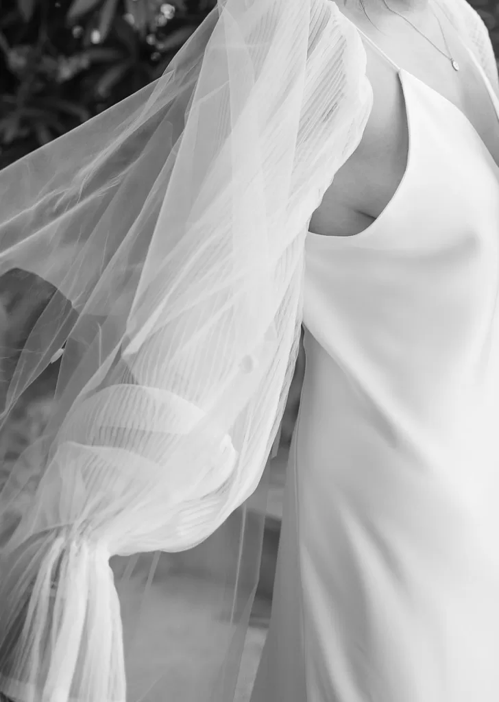 Close-up in black and white capturing the airy tulle sleeves and smooth satin texture of the bride’s gown.