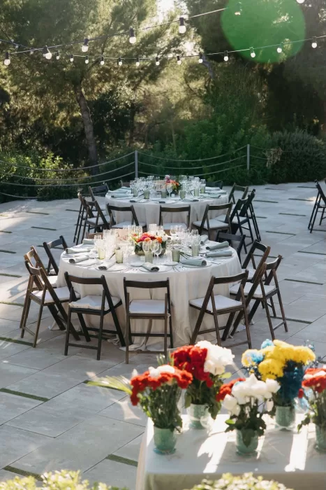 Elegant round tables with fresh florals and soft linens set for an outdoor wedding dinner at Masia Casa del Mar under string lights.