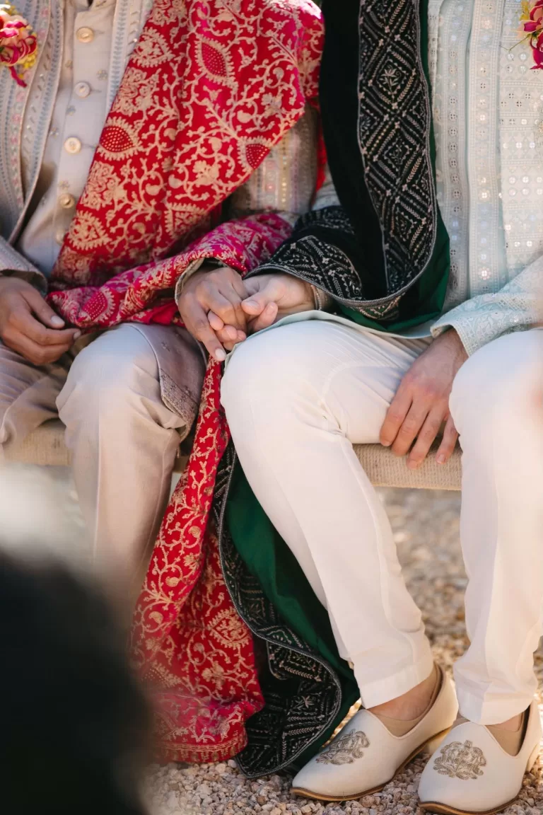 Two grooms holding hands during their wedding ceremony at Masia Casa del Mar, wearing traditional embroidered outfits.