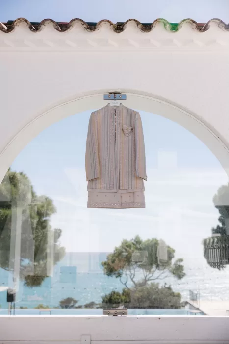 Pastel striped sherwani and embroidered kurta hung by an arched window overlooking the Mediterranean at Masia Casa del Mar.