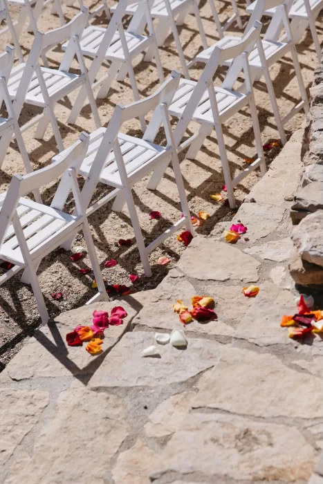 Scattered rose petals along a stone aisle between white ceremony chairs at Masia Casa del Mar.
