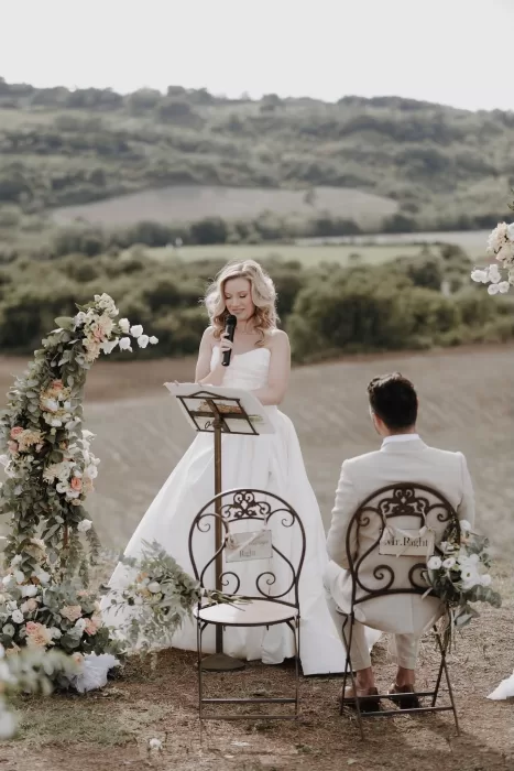 Bride reading her vows to the groom under a floral arch at Podere Calvaiola.