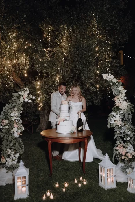 Newlyweds cut their floral wedding cake beneath twinkling fairy lights at Podere Calvaiola.