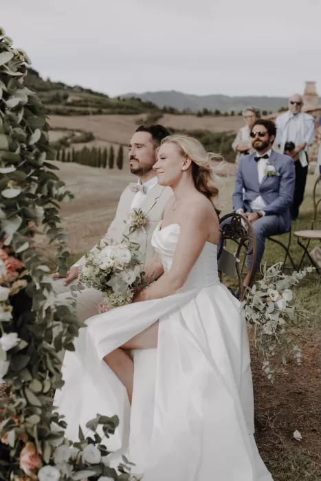 Bride and groom seated together during ceremony, surrounded by soft blooms at Podere Calvaiola.