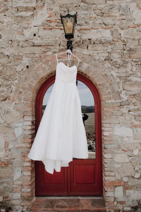 Elegant white wedding dress hanging against rustic stone wall at Podere Calvaiola.