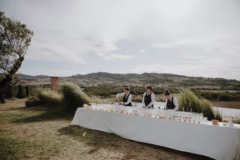 Outdoor drinks station with staff preparing refreshments against scenic countryside backdrop at Podere Calvaiola.