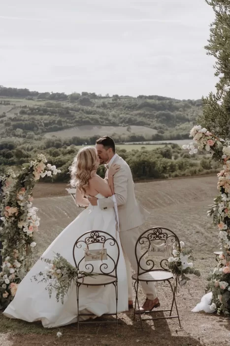 Bride and groom share first kiss surrounded by flowers and Tuscan landscape at Podere Calvaiola.