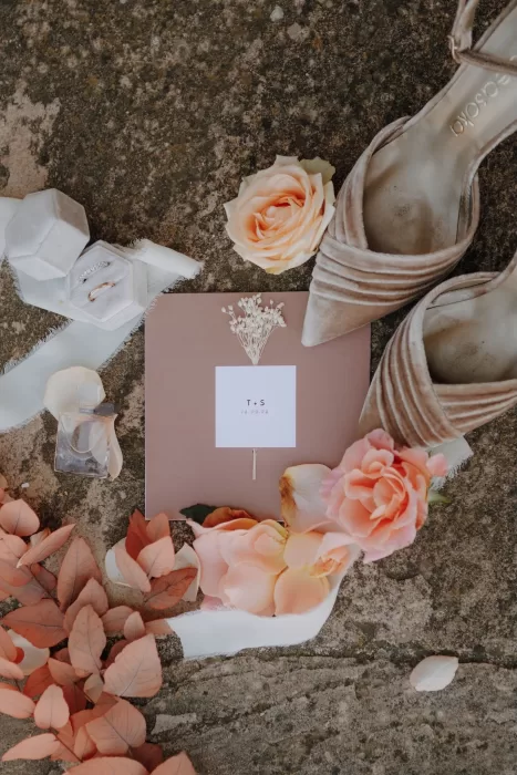 Romantic wedding flatlay with blush roses, velvet shoes, rings, and invitation at Podere Calvaiola.