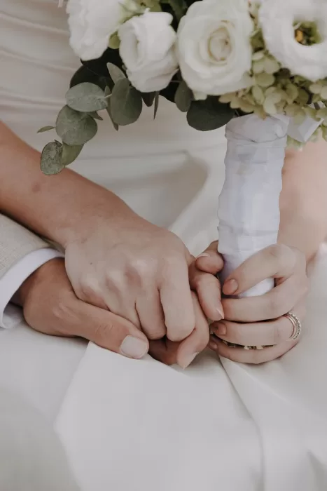Close-up of couple holding hands with bouquet resting in bride’s lap during Podere Calvaiola ceremony.