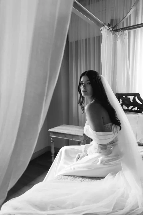 Emotional black and white portrait of the bride in her wedding dress sitting gracefully on a canopy bed at Tenuta Corbinaia.