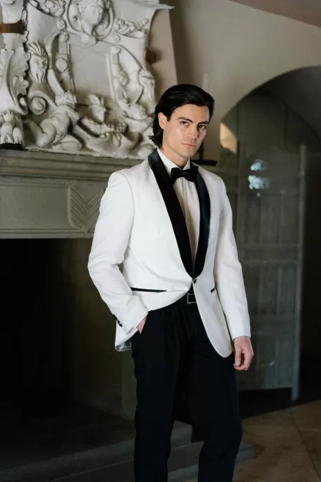 Groom in a white tuxedo jacket standing confidently indoors at Tenuta Corbinaia, exuding timeless elegance.