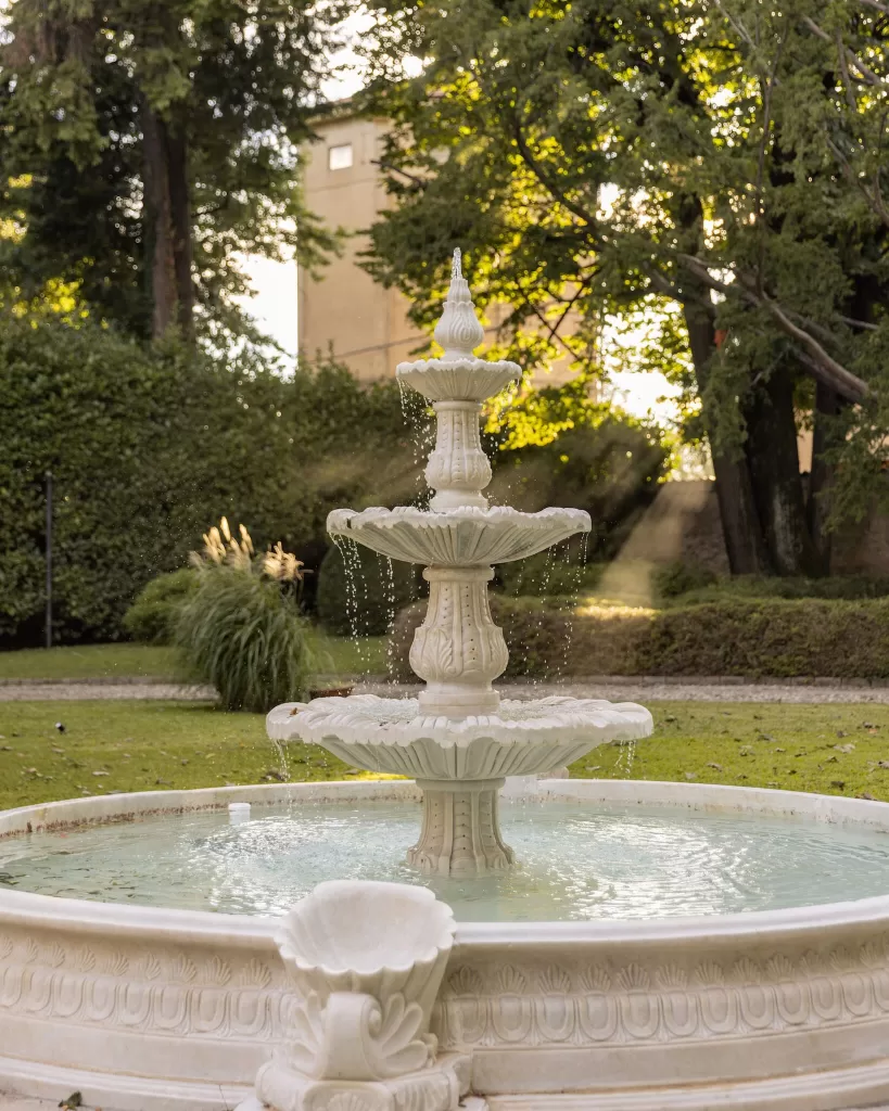Three-tiered white stone fountain in the lush garden at Villa Buttafava, with water sparkling in the golden evening light