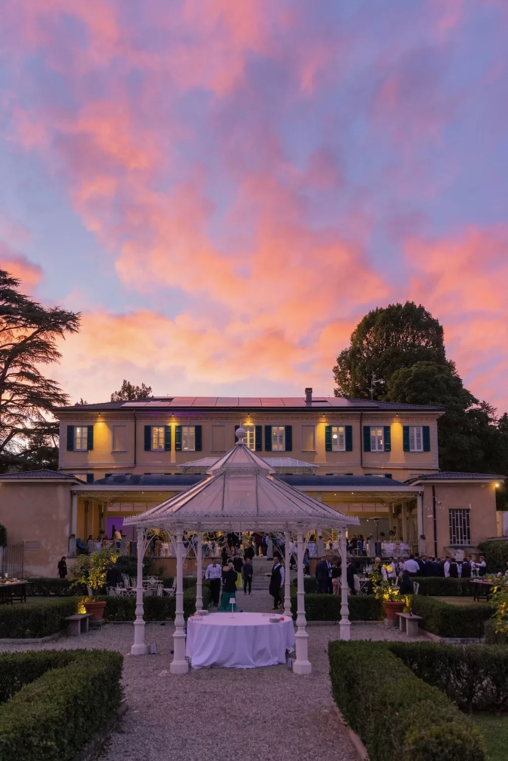 Wedding reception at Villa Buttafava during golden hour, with a glowing sky of pink clouds above the garden gazebo and historic villa facade.