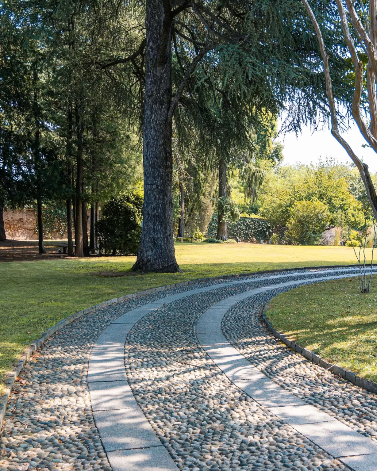 Curving stone path shaded by tall trees in the expansive grounds of Villa Buttafava