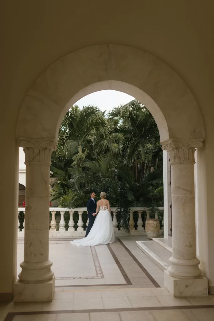 Bride and groom framed by a stone archway overlooking palm gardens at Villa La Joya.