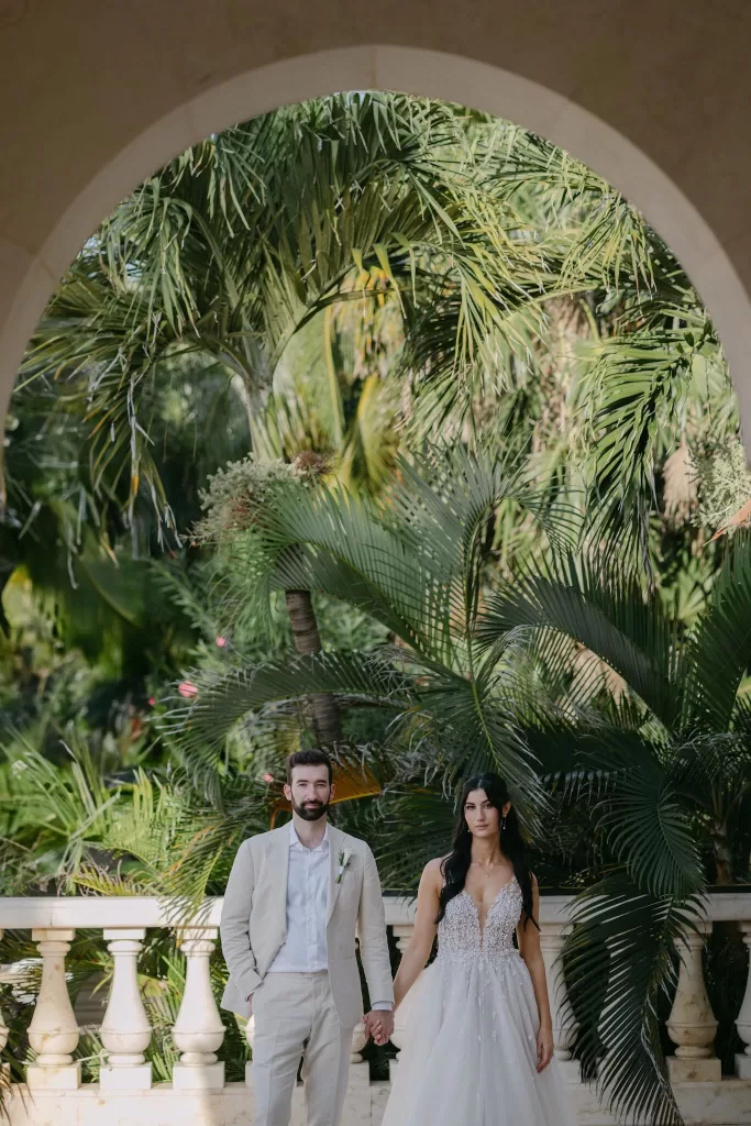 Bride and groom framed by a stone archway at Villa La Joya, surrounded by lush greenery.