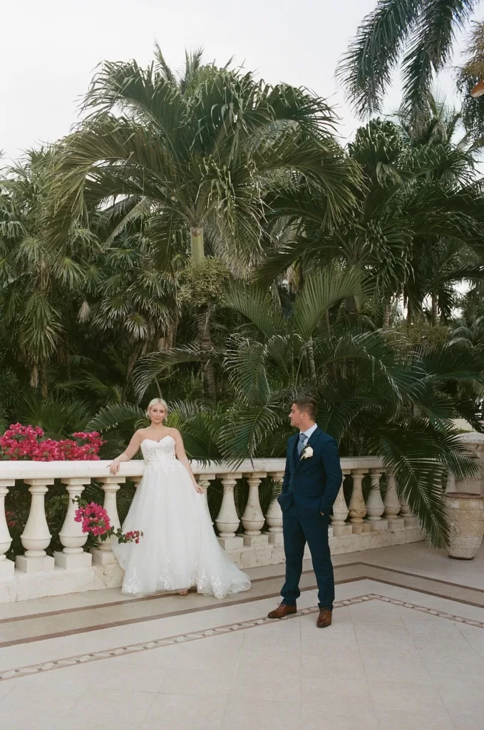 Bride and groom pose on a marble balcony surrounded by lush tropical palms at Villa La Joya.