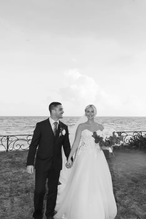 Bride and groom walking hand in hand by the ocean at Villa La Joya with joyful expressions.