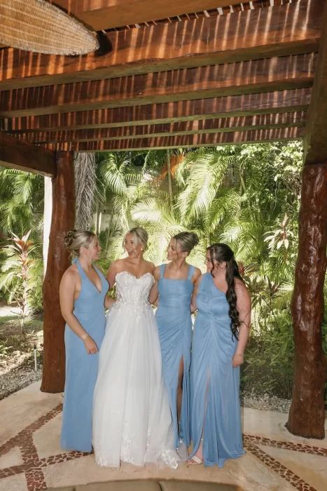 Bride shares a joyful moment with her bridesmaids in light blue dresses under a tropical pergola at Villa La Joya.