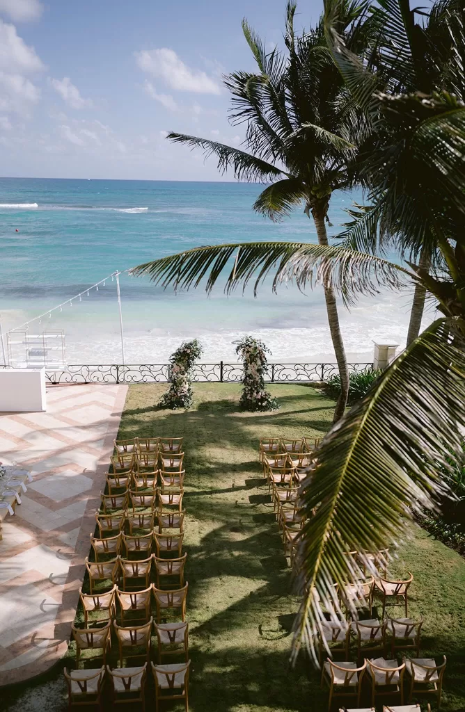 Oceanfront wedding ceremony lawn at Villa La Joya with wooden chairs and floral arch between palm trees.