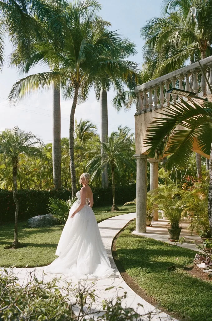 Bride walks along a palm-lined garden path beside stone columns at Villa La Joya