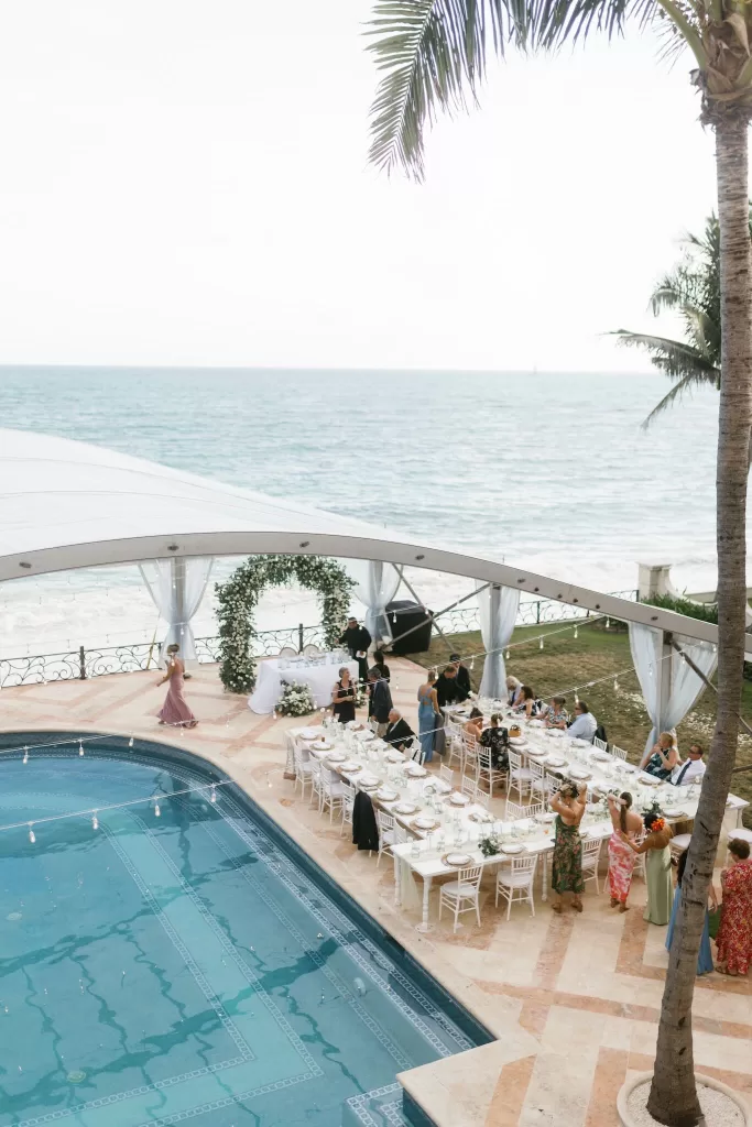 Elegant outdoor reception setup by the sea with a floral arch and long tables at Villa La Joya.