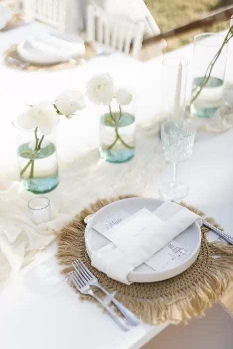 Refined beach wedding place setting with white roses and woven placemat at Villa La Joya.