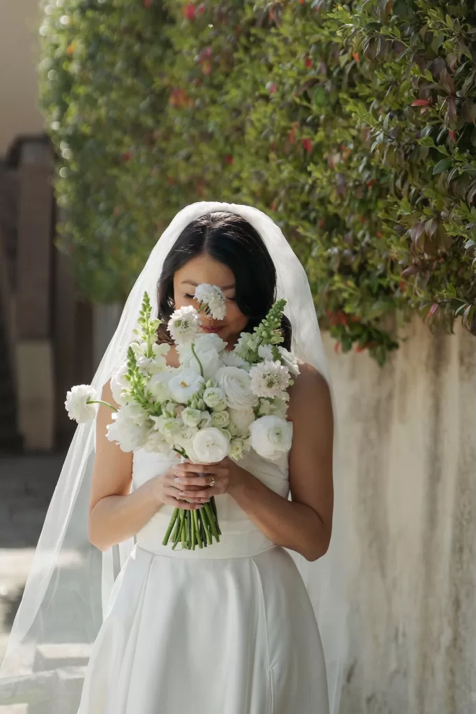 Bride in a strapless gown holding a soft white and blush bouquet at Villa Medicea di Lilliano, framed by sunlit greenery.
