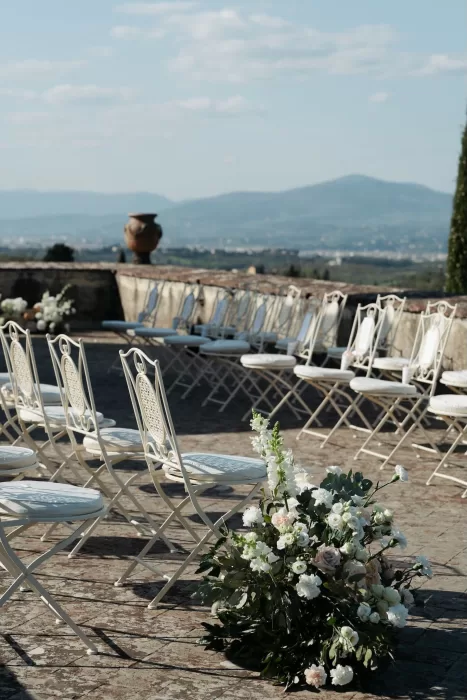 Elegant ceremony chairs and white floral arrangements on the panoramic terrace of Villa Medicea di Lilliano overlooking Tuscany.