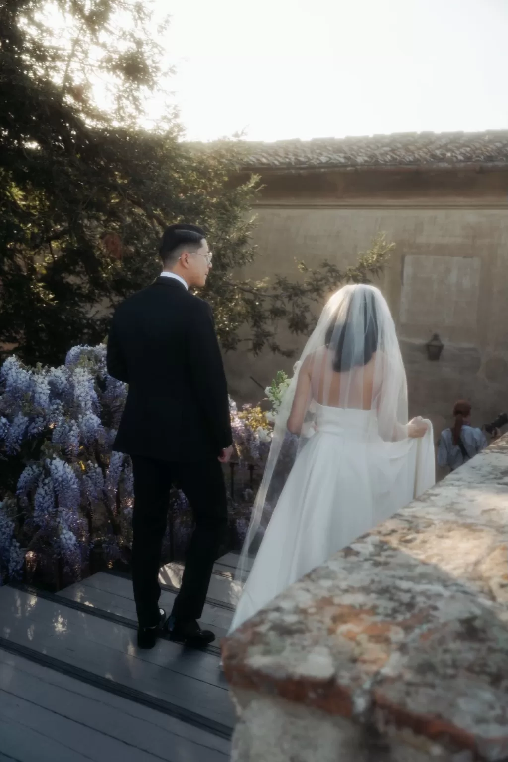 Bride and groom smiling together in front of blooming wisteria at Villa di Maiano.