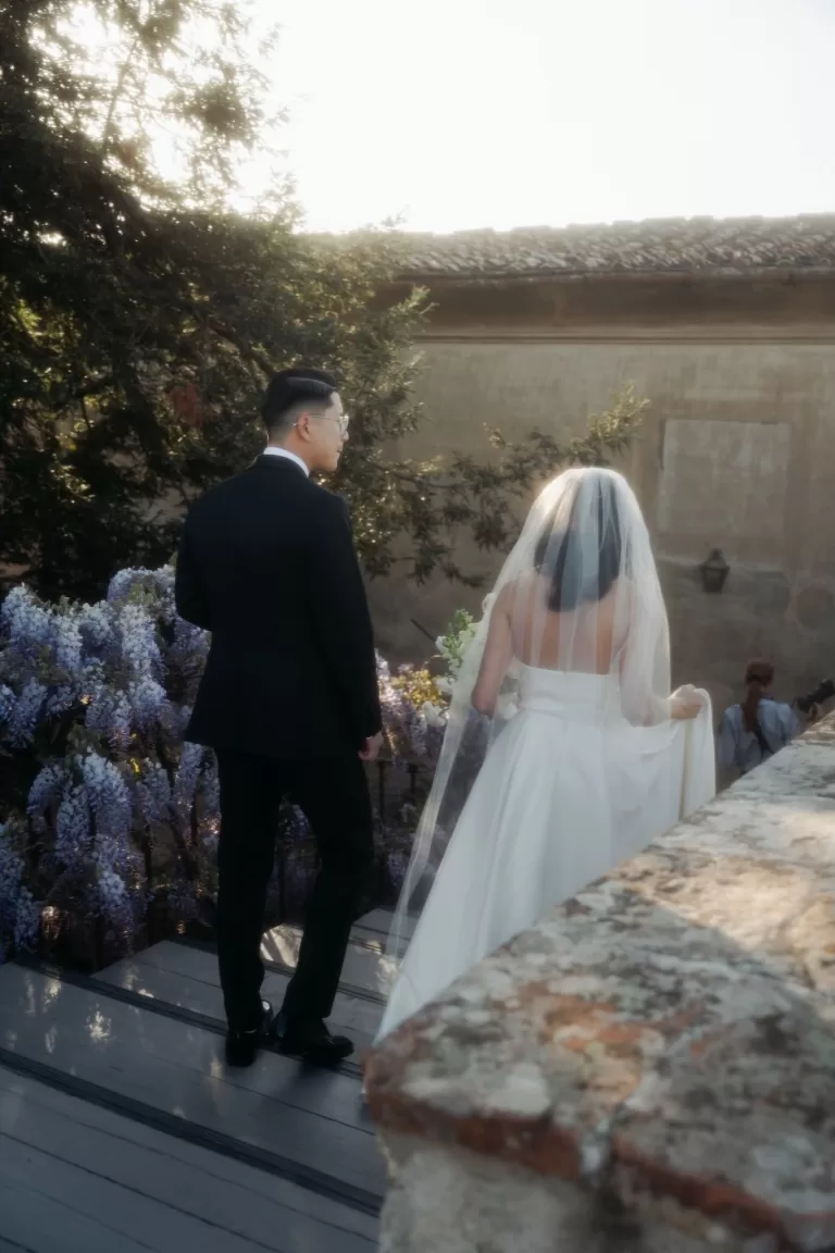 Bride and groom smiling together in front of blooming wisteria at Villa di Maiano.