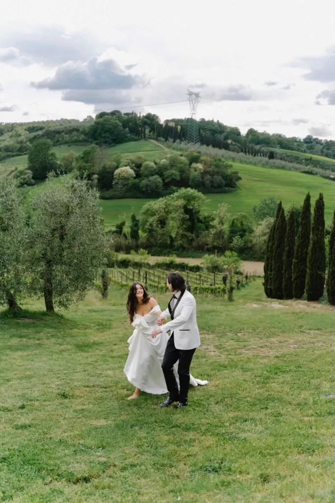 A joyful bride and groom walking barefoot through the vineyards at Tenuta Corbinaia, enjoying the rolling green hills.