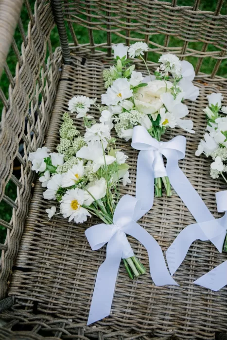 Delicate white bridal bouquets with satin ribbons arranged in a woven basket on the grass.
