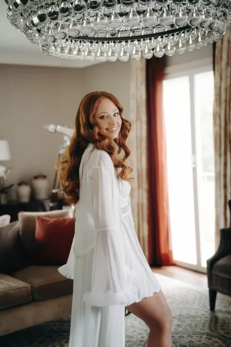 Bride with flowing red hair smiles while getting ready in a suite at Hotel Villa Honegg, surrounded by warm morning light.