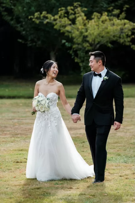 Bride and groom sharing a joyful moment while walking hand in hand on the Château Challain lawn.