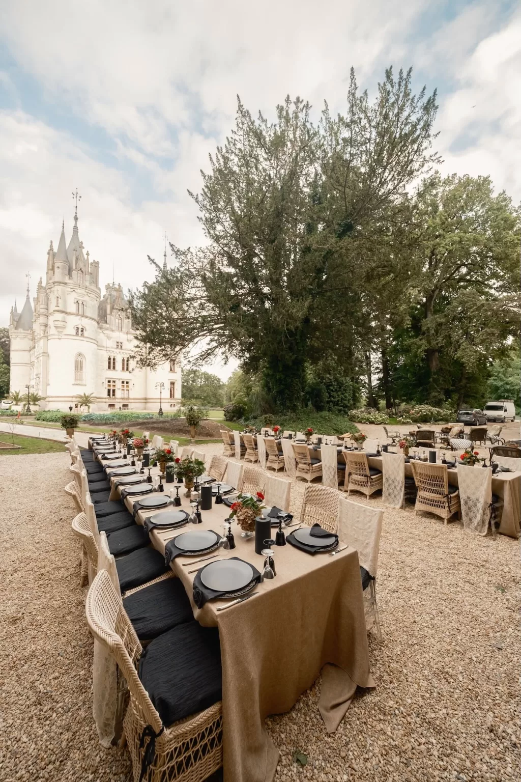 Wide-angle view of alfresco wedding dinner layout at Chateau Challain with black and neutral tones beneath towering trees.