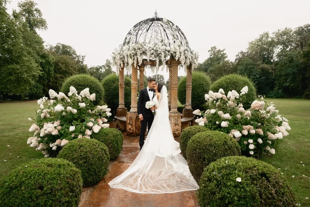 Romantic garden moment as the couple share a kiss under a flower-covered gazebo at Chateau Challain.
