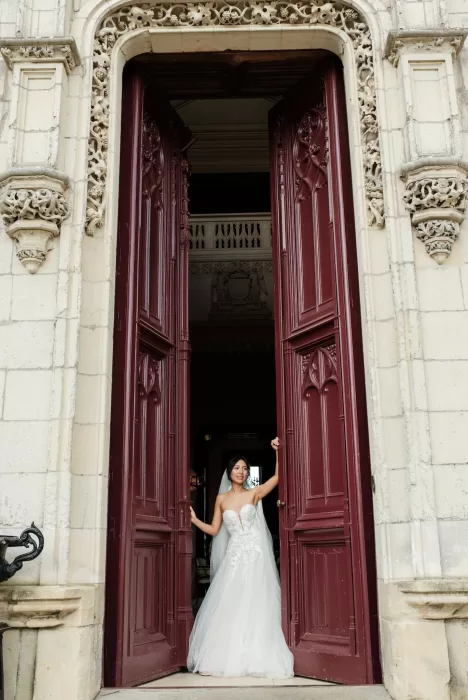 Groom in a tuxedo standing beside an ornate fireplace and mirror inside Château Challain’s opulent suite.