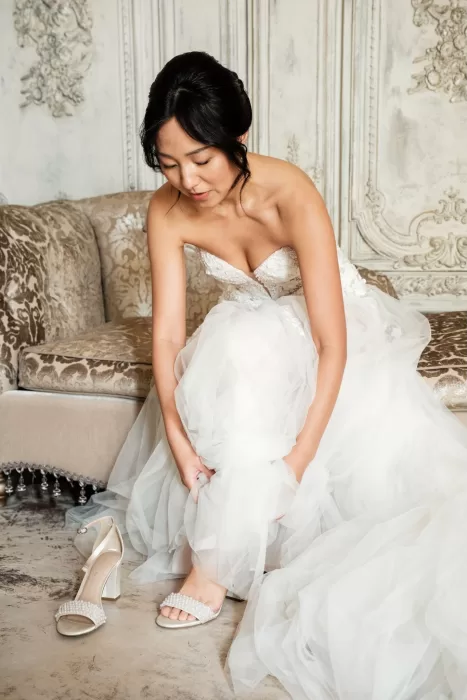Bride adjusting her shoes while seated on a plush sofa in an elegant suite at Château Challain.