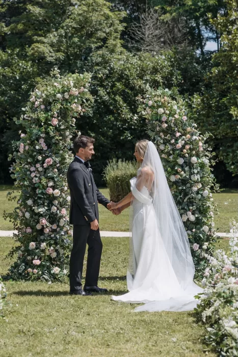 Couple holding hands beneath romantic floral arches during the ceremony at Château de la Couronne.