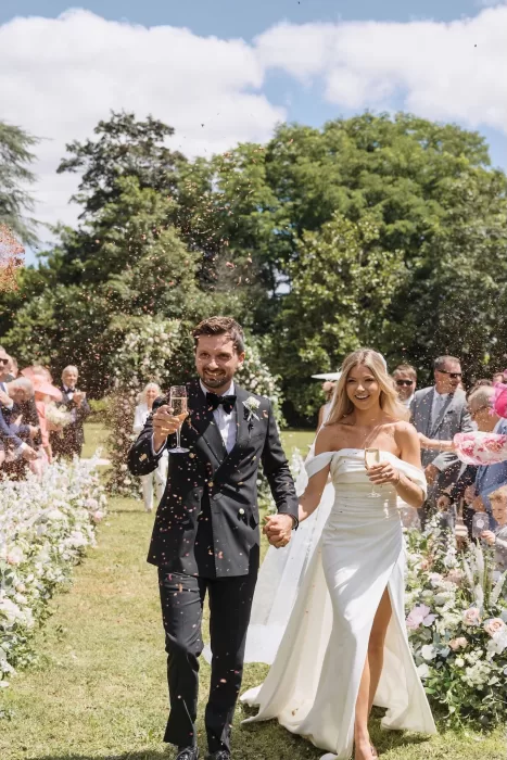 Joyful confetti toss as newlyweds walk down the aisle with champagne at Château de la Couronne.