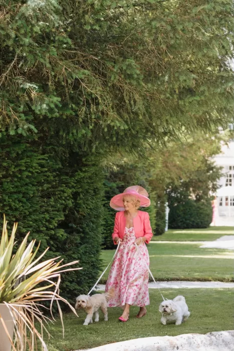 Wedding guest in a floral dress and hat arriving with two small dogs at Château de la Couronne.