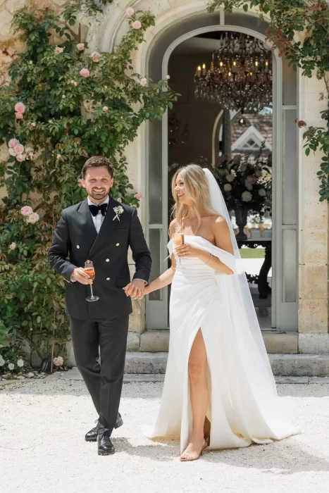 Newlyweds walking hand in hand and laughing outside Château de la Couronne on a sunny day