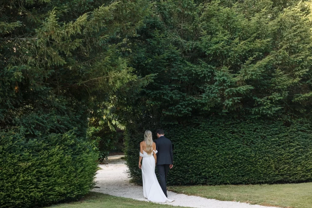 Newlyweds strolling down a shaded garden path surrounded by greenery at Château de la Couronne