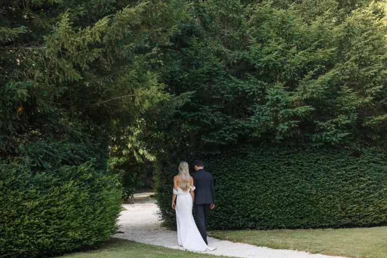 Newlyweds strolling down a shaded garden path surrounded by greenery at Château de la Couronne