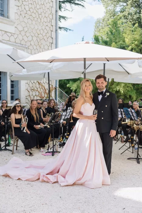 Bride and groom smiling beside a live band under parasols at Château de la Couronne