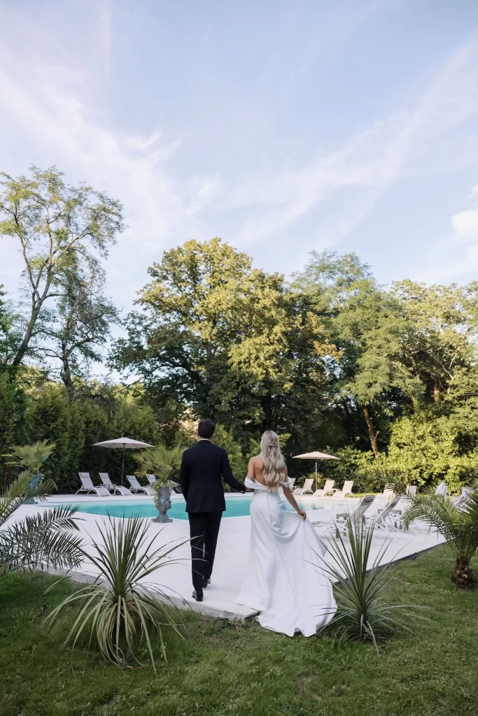 Bride and groom walking hand in hand beside the pool at Château de la Couronne