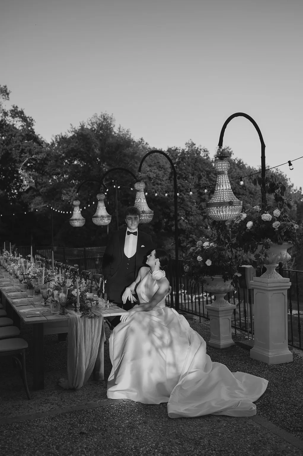 Bride and groom in black tie elegance beneath chandeliers at Château de Sanse