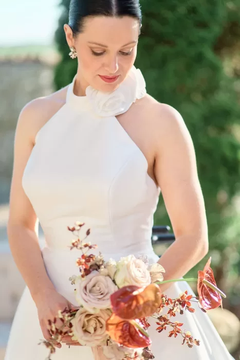 Bride in halterneck gown with floral neckline holding a modern bouquet at Chateau de Sanse.